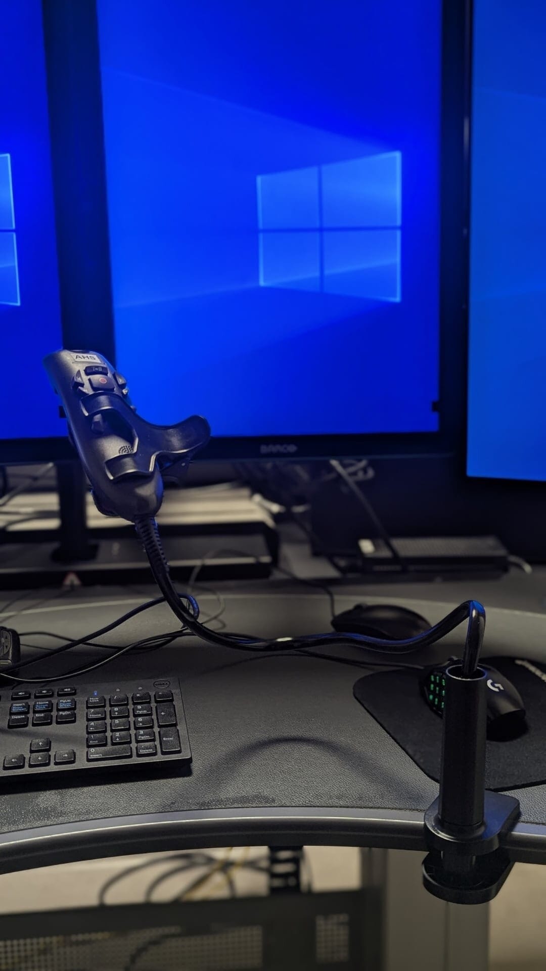 Front view of a Nuance PowerScribe microphone on a gooseneck holder with dual monitors displaying Windows desktop.